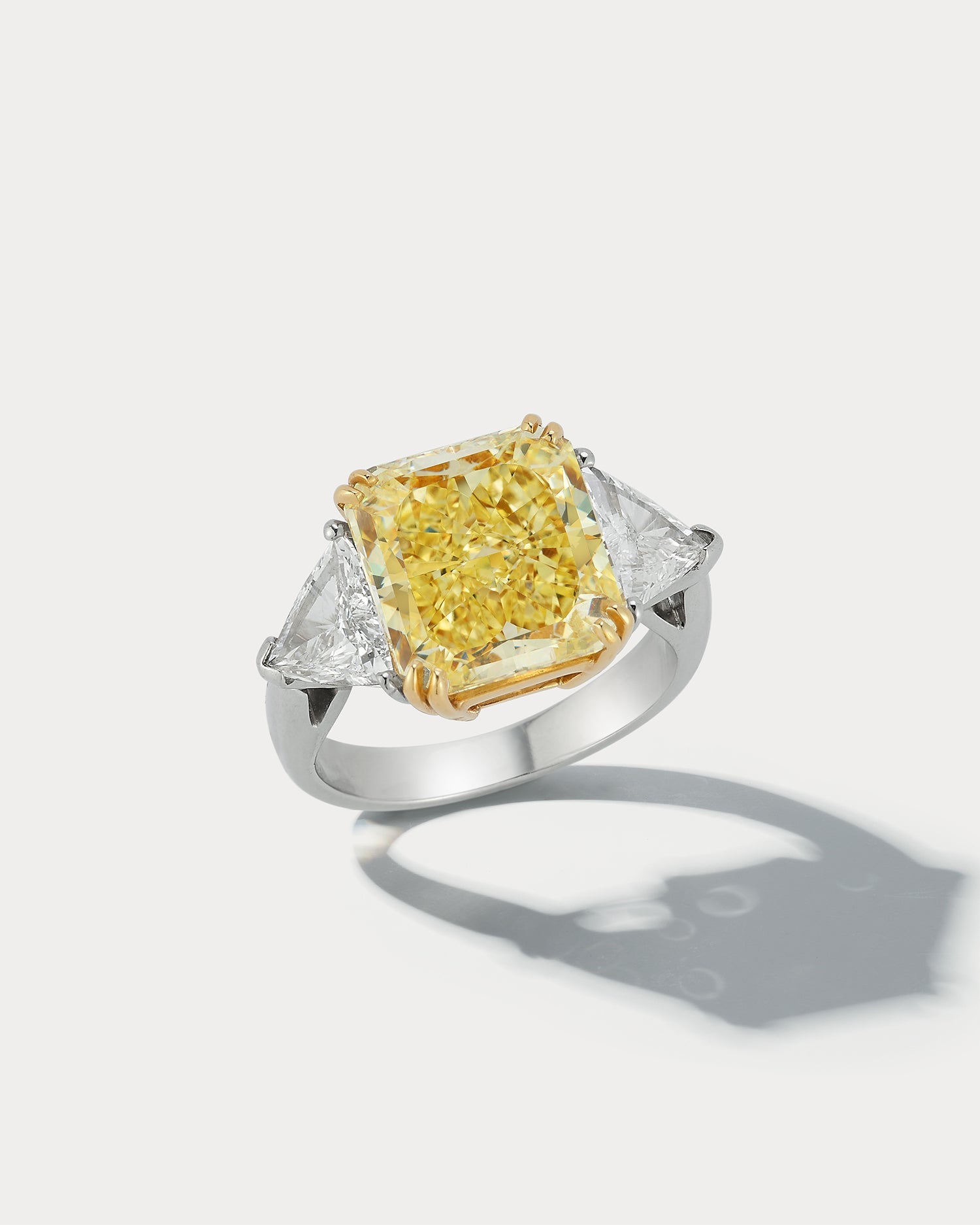 Ammrada 7.49 carat Fancy Yellow Radiant-cut three-stone ring showcasing a large yellow center stone with side stones.