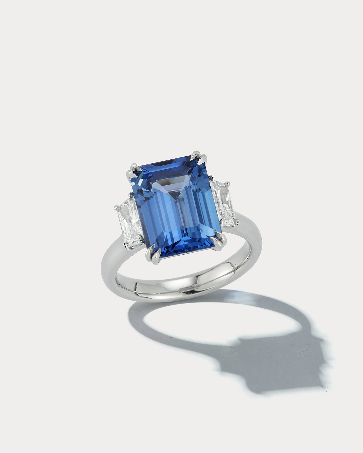 Ammrada three stone ring featuring a 6.93 carat emerald-cut sapphire center stone with side sapphires on a silver band.
