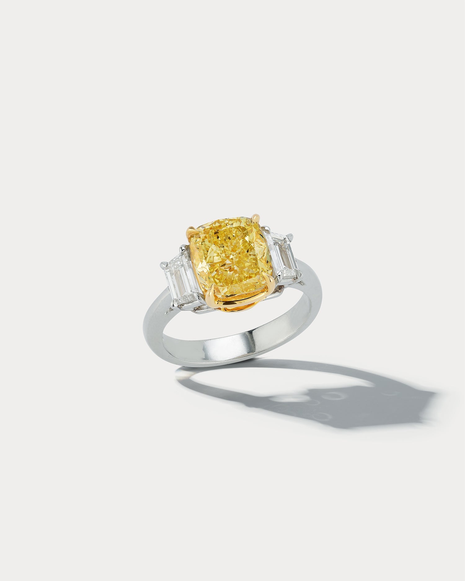 Ammrada 4.01 carat fancy intense yellow cushion-cut center stone three-stone ring displayed on a ring holder.